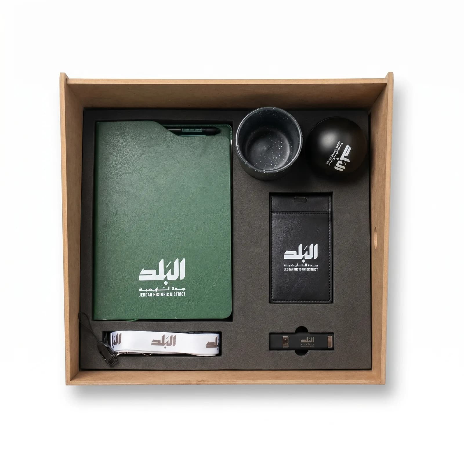 طقم ترحيبي لبرنامج جدة التاريخية في صندوق خشبي: دفتر جلدي أخضر، وكوب، وحافظة بطاقة، وحبل تعليق، تنفيذ فيستا يونايتد.